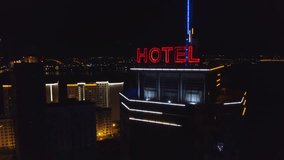 AERIAL: Neon red inscription hotel on the roof of a modern building in the night city. Traffic cars are next on the road. The word hotel on the roof of a skyscraper. - Powered by Shutterstock - Get 15% off with code: PIKWIZARD15