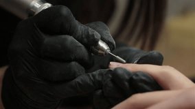 Closeup shot of hardware manicure in a beauty salon. Manicurist is applying electric nail file drill to manicure on female fingers.
