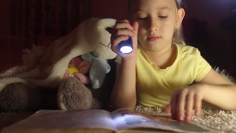 Little Girl is Reading a Book With Flashlights at Night. Happy Girl Plays at Home. Funny lovely kid having fun in children room.