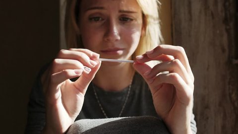 Crying woman sitting on the windowsill about positive pregnancy test result