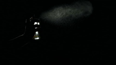 Close-up silhouette of a girl spraying perfume in the dark, slow motion.