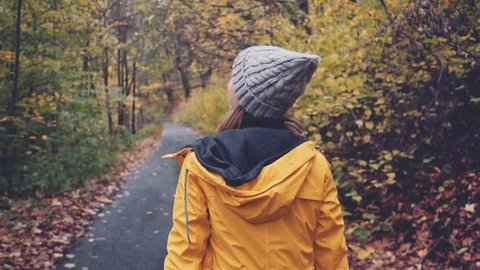 Woman Walking through Autumn Forest. SLOW MOTION 120 FPS, STABILIZED SHOT. Girl in yellow raincoat and knitted hat enjoying fall day outdoors, walking through woodland.  Disconnected concept. 
