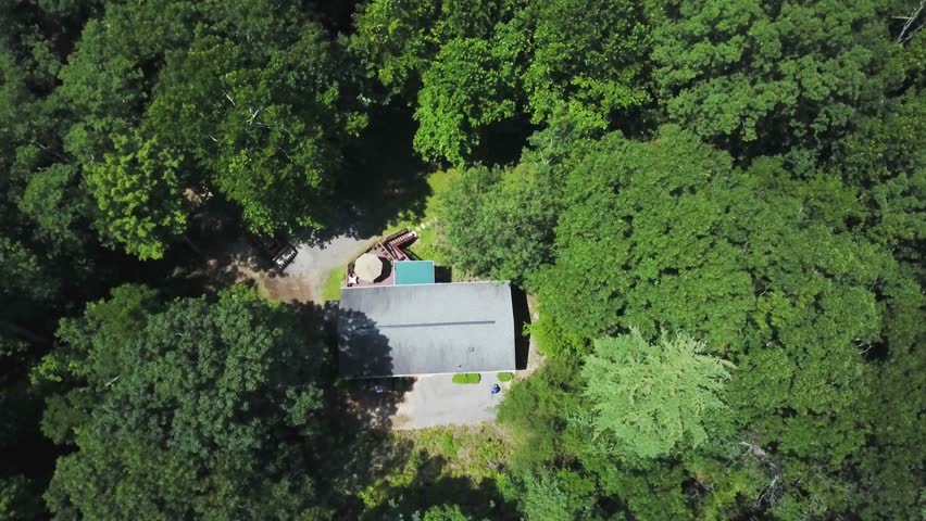 Descending camera onto a view of a house in the forest with a worker smoothing gravel out as part of a landscaping