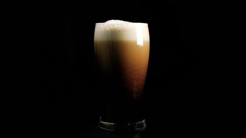 A pint of dark beer foam beautifully against black background