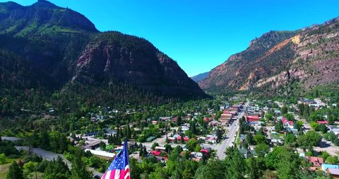 American Flag Waving In The Breeze Above Colorado Town In Mountain Valley Surrounded By Green Pines - Ouray, Colorado, USA