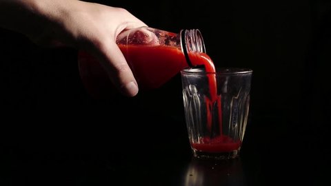 Men's hands pour cold tomato juice from the plastic bottle into a glass. Healthy lifestyle concept. Bloody Mary cocktail preparing. Closeup isolated shot.