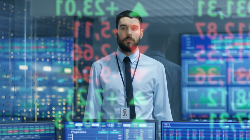 Stock Market Top Trader Looks at Projected Ticker Numbers and Graphs Running, Analysing Data to Make Best Sell. Behind Him Room Full of Screens and Statistics. Shot on RED EPIC-W 8K Helium Camera.