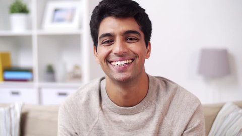 emotion, expression and people concept - portrait of happy smiling young indian man at home