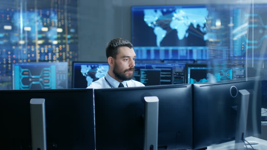 In the System Control Center Technical Operator Monitors Displays at His Workstation. He's Surrounded by Displays Showing Relevant Data. In the Background Data with Interactive Map.  | Shutterstock HD Video #32307757