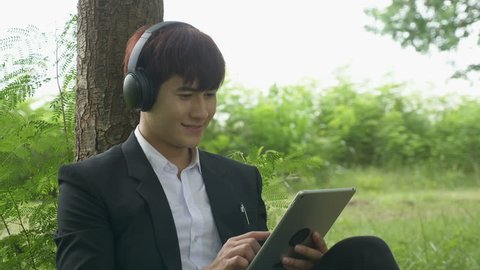 Asian Young male listening to music with wireless headphones in autumn park