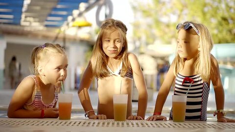 three children is having fun in a water park in summer, standing near an edge of pool with juicy drinks