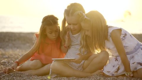 children on a beach are playing with modern device, watching cartoons and playing in apps