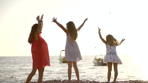 three little girl is playing on a sea shore in summer time, they are throwing stones to a water