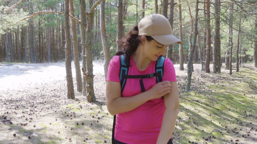 Woman in the park bitten by a mosquito. Young female in the woods waved off insects. Tourists with a backpack bite mosquitoes. Mosquitoes bite the tourist with a backpack.