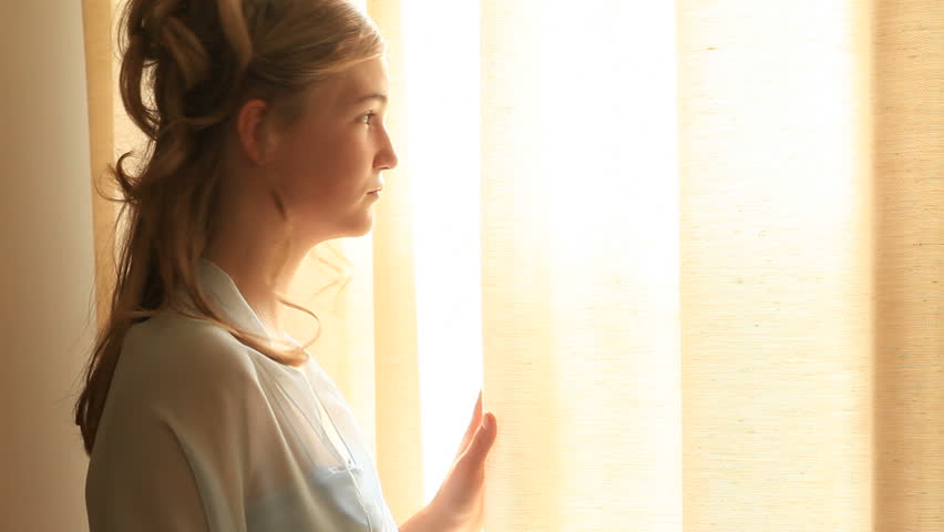 Beautiful young teen girl looking out of window. Young blond youth longingly looking out of window for her prince. Young girl day dreaming while lookin out of window. 