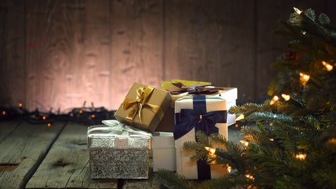Santa Claus puts gifts under the Xmas tree decorated with blinking garlands. Santa Claus giving gift box, holding a gift in his hands over wooden background. 4K UHD video