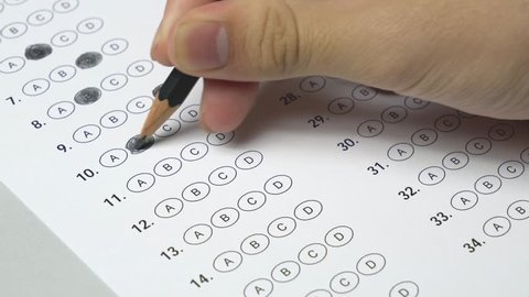 Student hand testing doing examination test with standardized test form and answers bubbled. Student filling out answers.