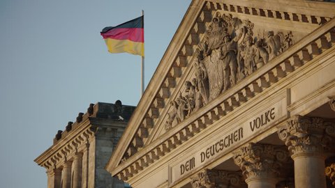 May, 2017 Berlin, Germany. Reichstag entrance inscription, sculptures, and German Flag on the front during sunset.