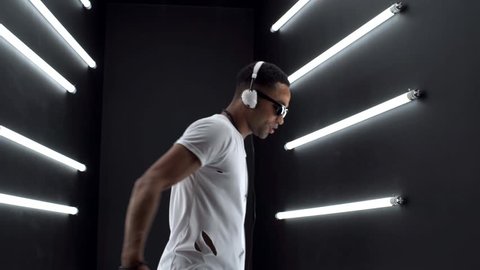 young hipster handsome black man dancing hip hop style, listening to music on headphones, close up legs, sneakers, neon light, disco party club, white apparel, smiling, happy, having fun, positive