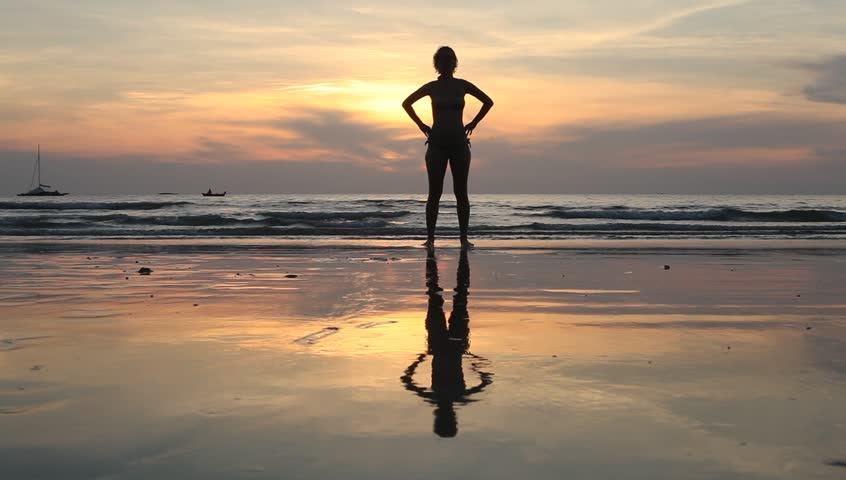 Young woman performs exercises on the beach during sunset.