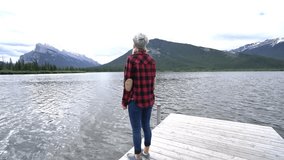 Young couple on a lake pier in Banff national park, Canada walked by the lakeshore and outstretches arms for positive emotion and success. People love travel outdoors concept
