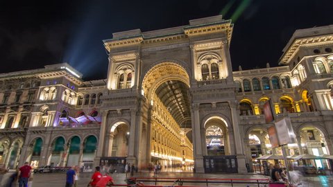 Night view of illuminated Vittorio Emanuele II Gallery timelapse hyperlapse in Milan, Italy. People walking on Square Piazza Duomo near entrance.