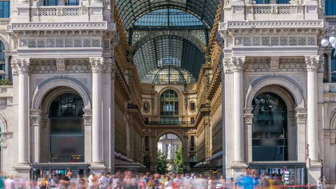 Entrance to the Galleria Vittorio Emanuele II timelapse on the Piazza del Duomo (Cathedral Square). This gallery is tourist attraction of Milan. Blue cloudy sky at summer day. People walking inside