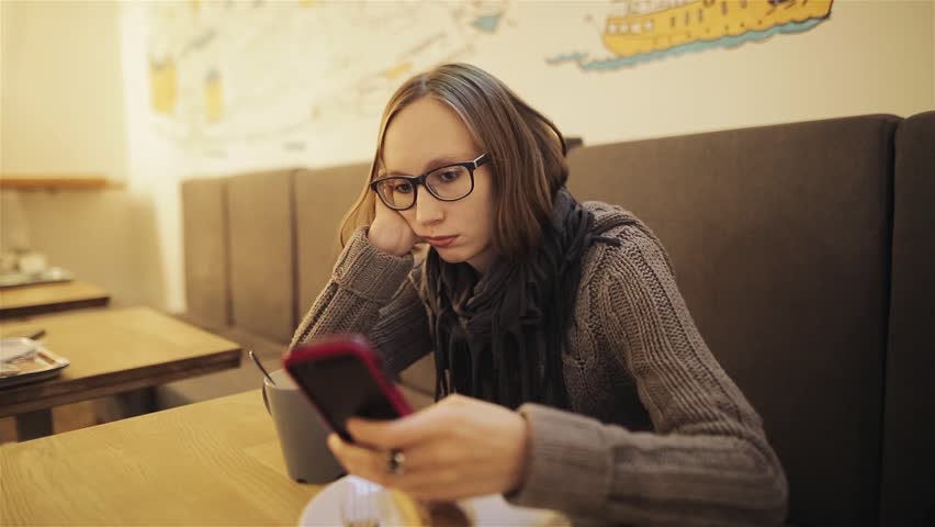 A frustrated young girl in glasses misses the cafe. The tired woman is waiting for the boyfriend and is bored with the phone in her hands. Love and relationships. Royalty-Free Stock Footage #32374288