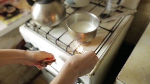 A young woman lights of a gas cooking plate with matches on the kitchen. Girl heating milk in a pan for oatmeal. Healthy foods, eating, diet concept. Cooking process.