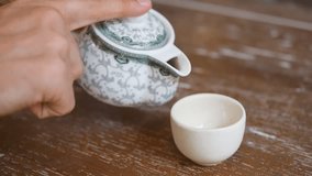 Male Hand Pouring Healthy Green Tea from Teapot in Vintage Cup on the Wooden Table. Traditional Chinese Ceremony Concept. HD, Slow Motion 180fps.