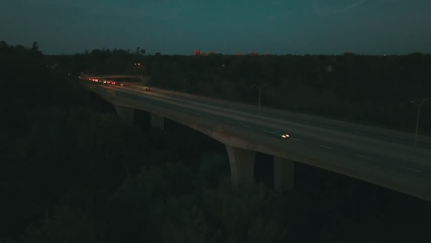 Aerial drone footage over a four lane bridge with sparse car traffic driving underneath.