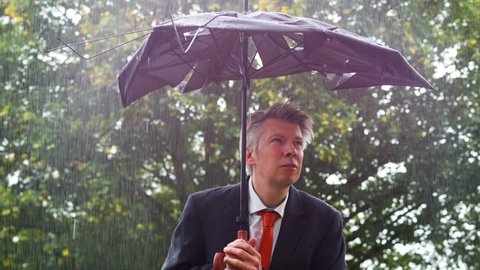 Businessman sheltering underneath a broken umbrella in the rain