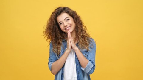 Happy shocked curly woman in denim shirt rejoice and clapping over yellow background