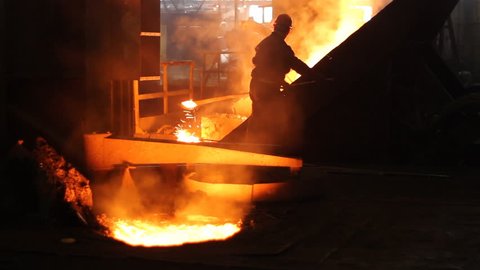 Hard work in the foundry, workers controlling iron smelting in furnaces, too hot and smoky working environment