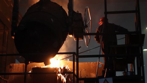 Hard work in the foundry, worker controlling iron smelting in furnaces, too hot and smoky working environment