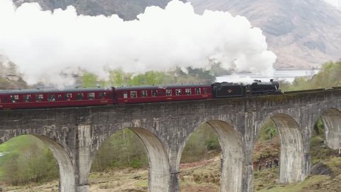 GLEN FINNAN, SCOTLAND - AUGUST 2017: Stunning aerial shot of the Jacobite steam train going over the Glenfinnan viaduct with white steam