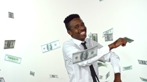 Slowmo of laughing African-American businessman in shirt and tie dancing against studio backdrop as money falling on him from above