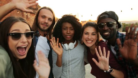 Multiethnical friends making selfie and waving their hands to the camera at the rooftop party. Urban. The sunset background. Outside. Stockvideo