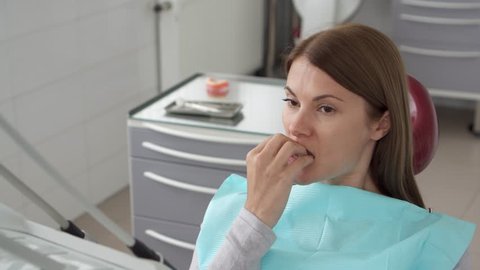 Woman patient in dental clinic. Waiting in dental chair for professional doctor stomatologist. Anxious, afraid, biting her nails. Dental equipment on background. Dental check up