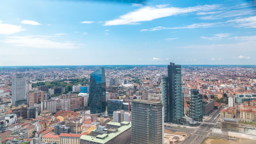 Milan aerial view of modern towers and skyscrapers and the Garibaldi railway station in the business district timelapse fiew from rooftop. Houses with red roofs. Blue cloudy sky at summer day