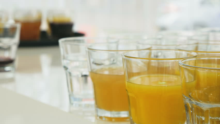 Grape juice being poured into a cup sitting amidst other cups that are already full with different kinds of juice. 