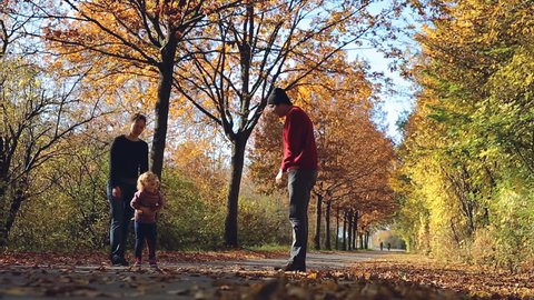 Mother, daughter, and father playing in an park on a road covered with fallen leaves. 