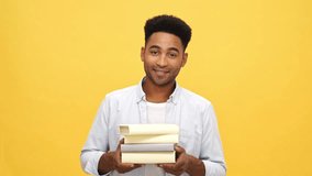 Smiling african man in shirt holding many books and looking at the camera over yellow background