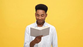 Cheerful african man in shirt holding and reading book over yellow background