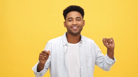 Pleased african man in shirt dancing and looking at the cameraPleased african man in shirt dancing and looking at the camera over yellow background over yellow background