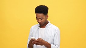 Concentrated african man in shirt writing message on smartphone and angry after that over yellow background
