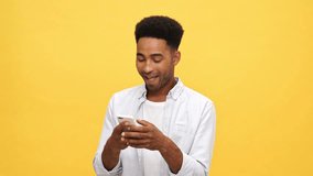 Smiling african man in shirt writing message on smartphone and upset after that over yellow background
