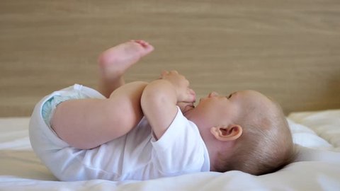 Lovely baby lying on bed play with feet and eat soles, tasting time