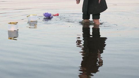 Beautiful festive ceremony - unidentified woman putting water lily flashlight with candle cast into the water down the river on warm summer evening - Βίντεο στοκ