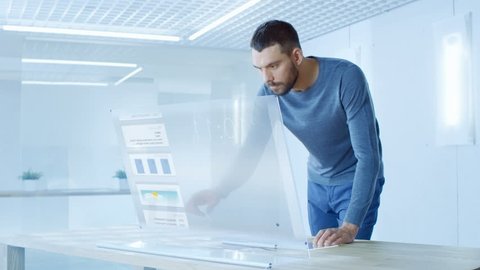 In the Near Future Stylish Man Logins in His High-Tech Computer with Transparent Display and Checks Useful Work Related Statistics. He Works in the Ultramodern Light Office. 4K UHD.